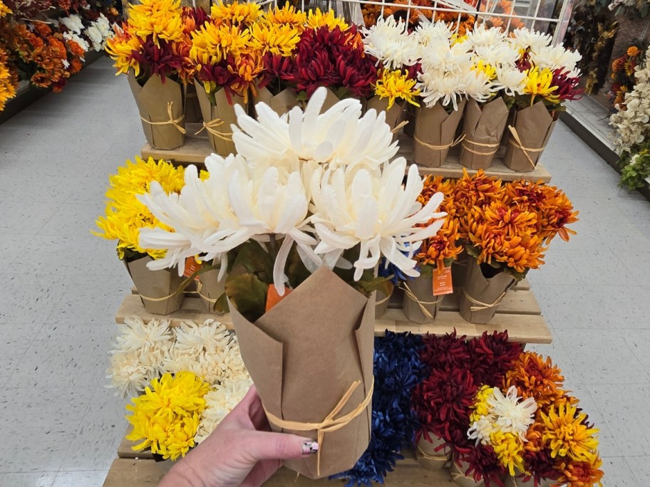 hand holding white mums in a paper wrapped pot