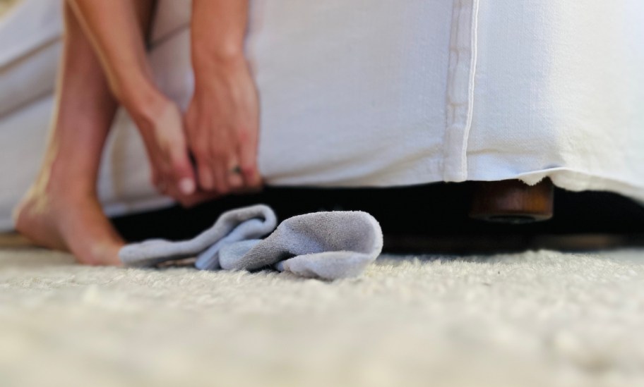 hands holding up sofa with dirty socks on carpet