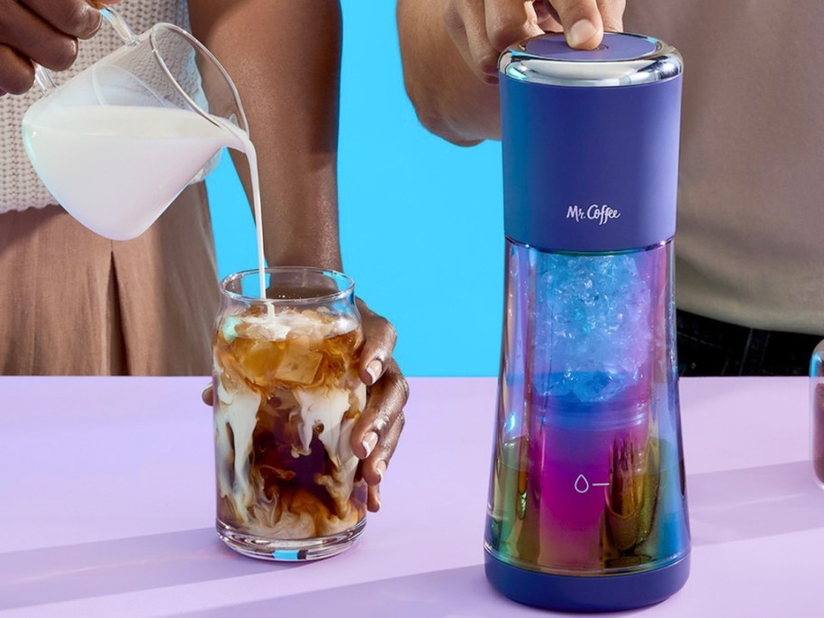 hand pushing on mr coffee maker while another person pours milk into drink 