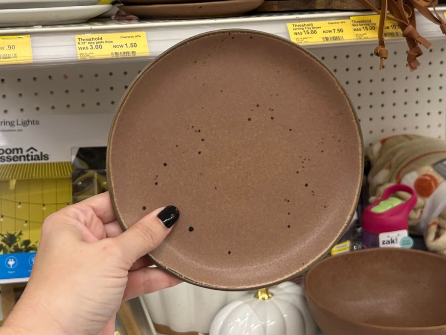 hand holding a brown stoneware style appetizer plate, store shelf with more plates behind it