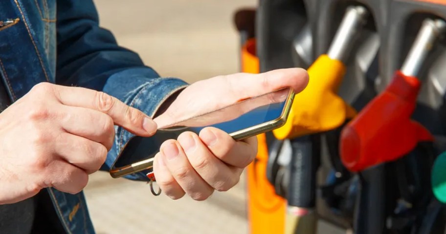 hand holding phone next to gas pumps