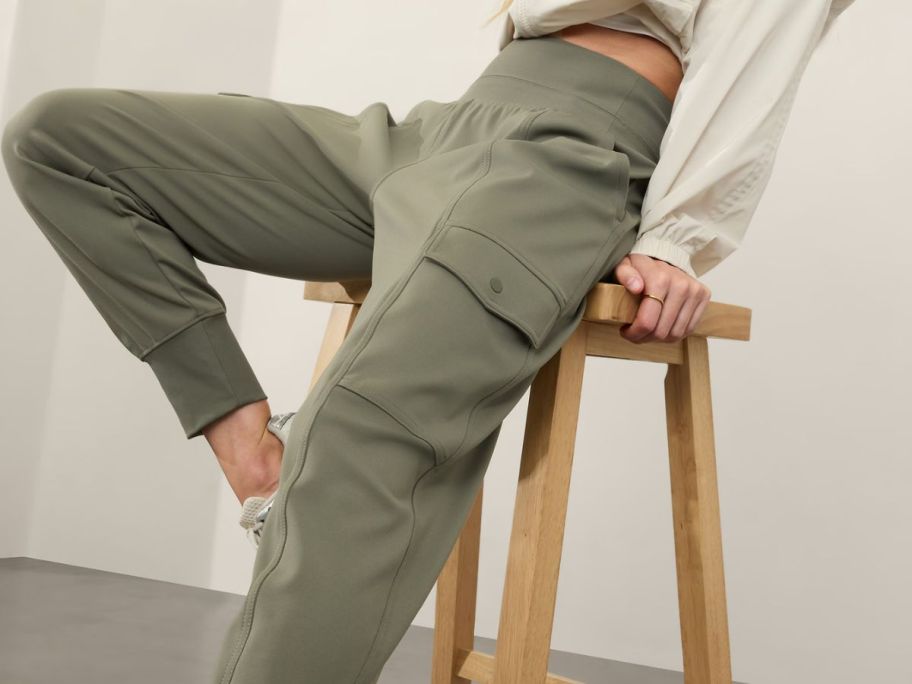 woman sitting on a stool wearing Athleta Venice High Rise Cargo Jogger in Moss 