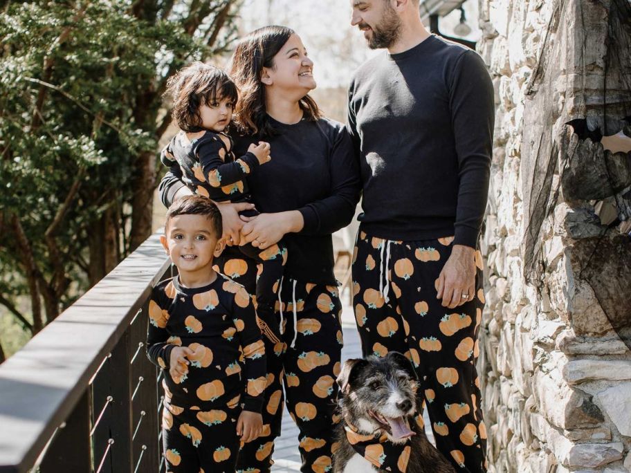 A mom, dad, and two kitds wearing Burt's Bees halloween pajamas with their dog wearing a matching bandana