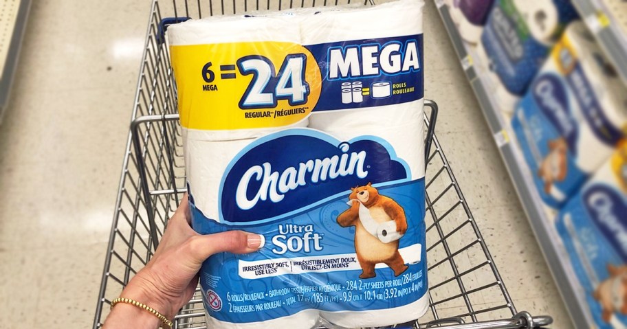 hand holding a blue pack of Charmin Ultra Soft Toilet Paper in front of shopping cart