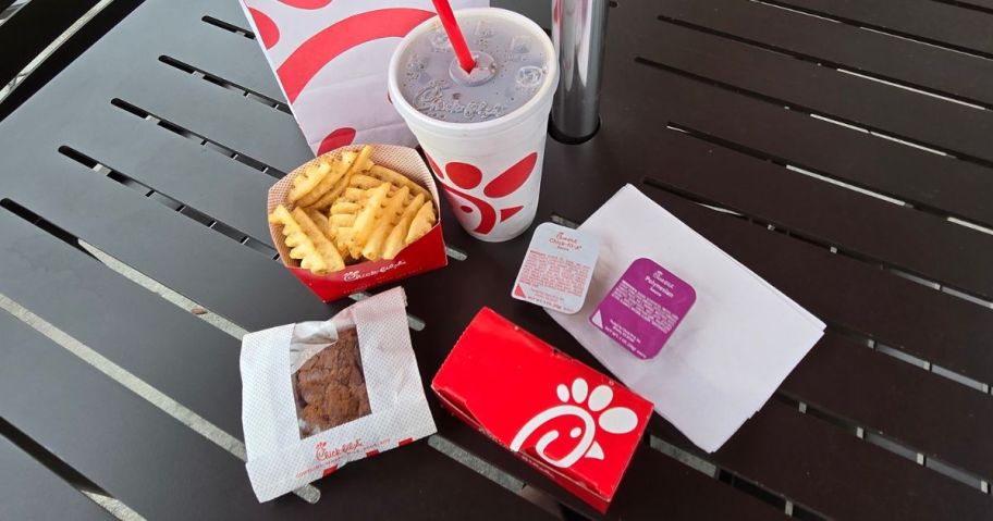 A table with Chik-Fil-A food items including fries, brownie, nuggets, soda and sauce