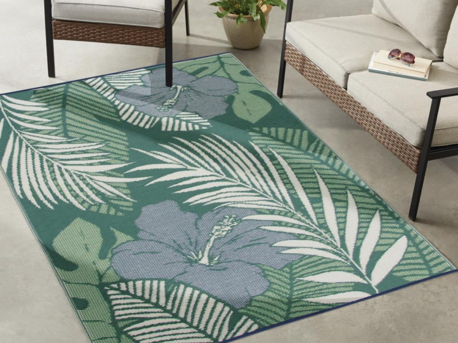 Green and blue outdoor rug with palm tree leaves, and flowers in front of beige couch