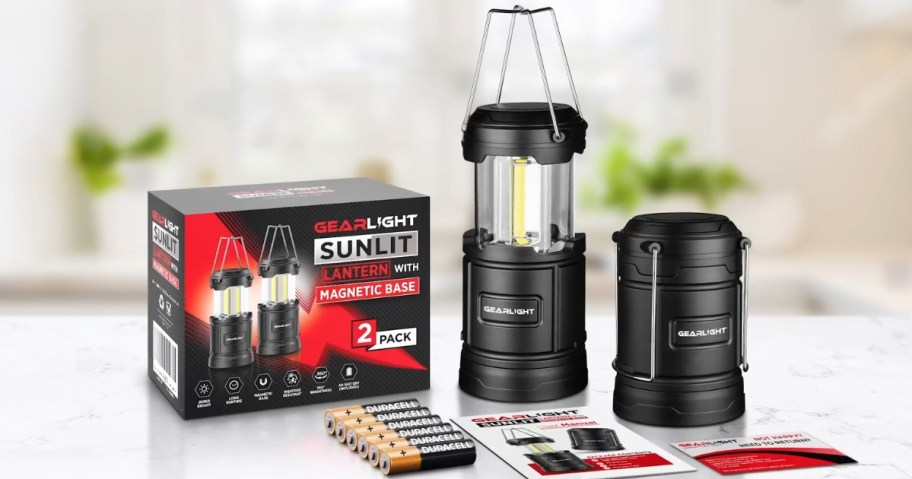 2 black camping lanterns with batteries, the box they come in and instructions on a table