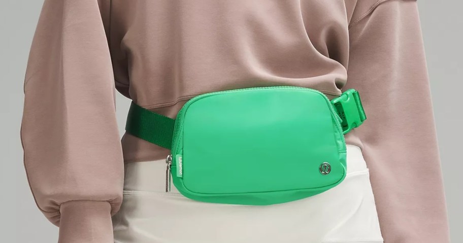 woman wearing a bright green lululemon belt bag around her waist with a tan long sleeve top and white skirt