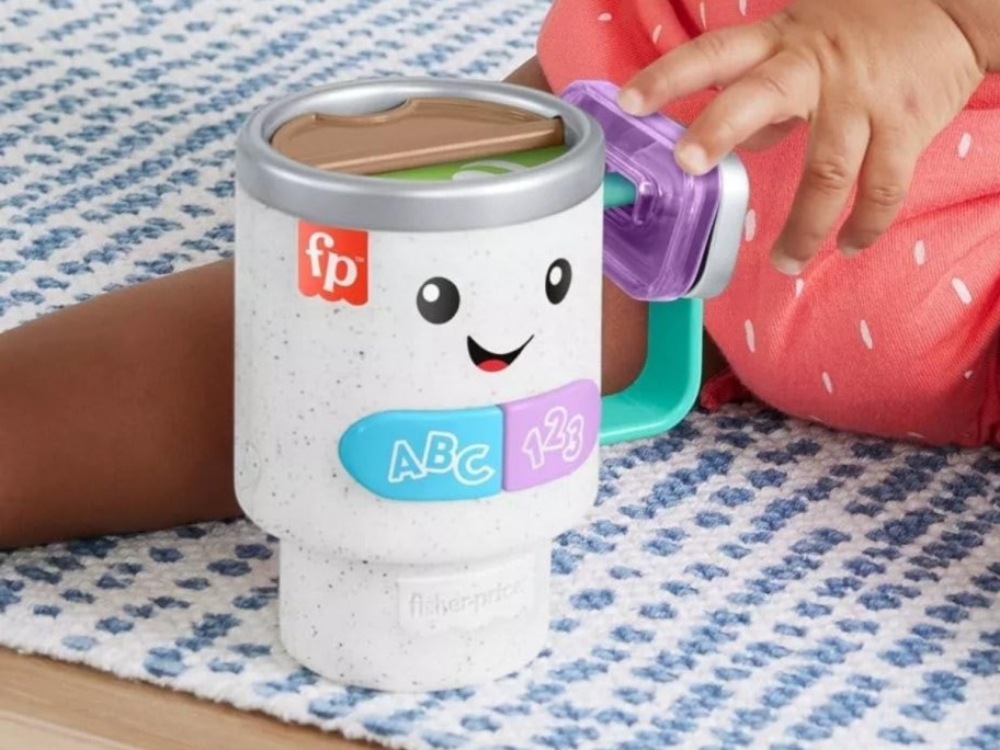 baby's legs on a rug playing with a white speckled, blue, purple, and green Fisher-Price Laugh & Learn Wake Up & Learn Coffee Mug