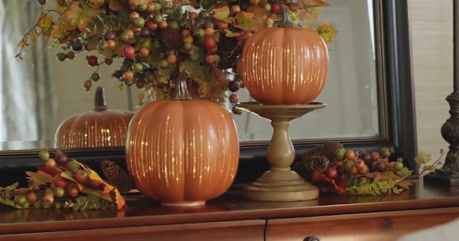 2 orange decorative pumpkins lit up with gold glitter accents on a fall mantle display