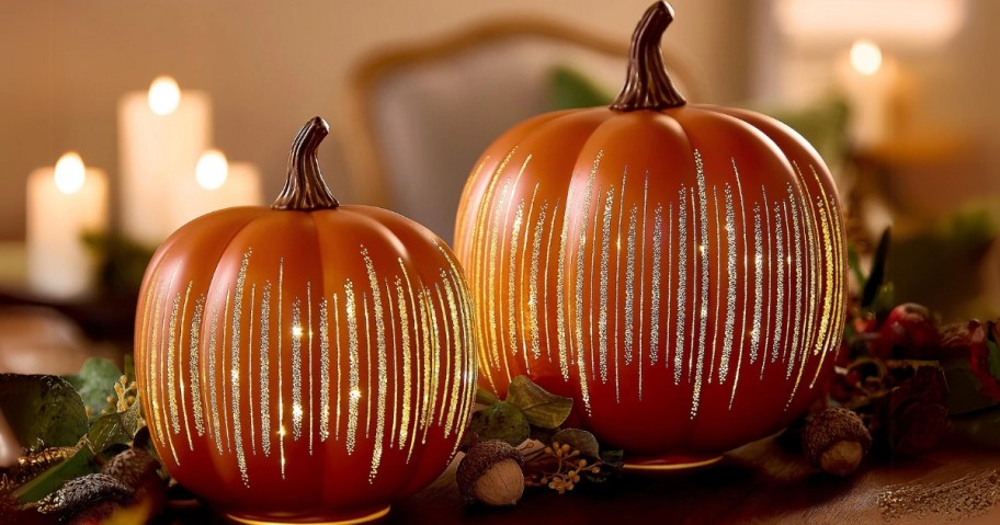 2 orange decorative pumpkins lit up with gold glitter accents on a table 