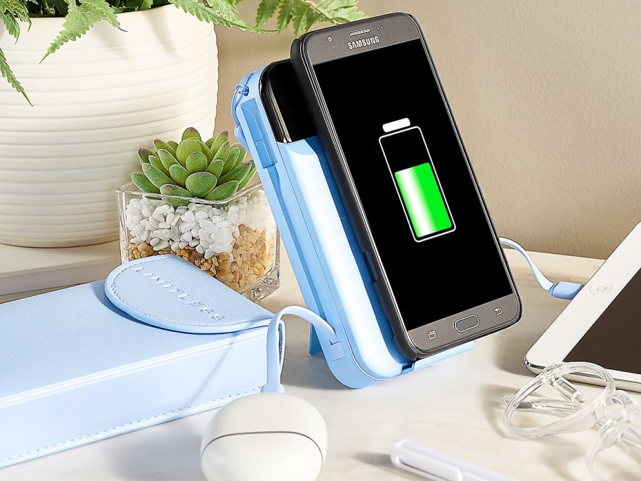 phone wirelessly charging on blue power bank with tablet and wireless earbuds also connected