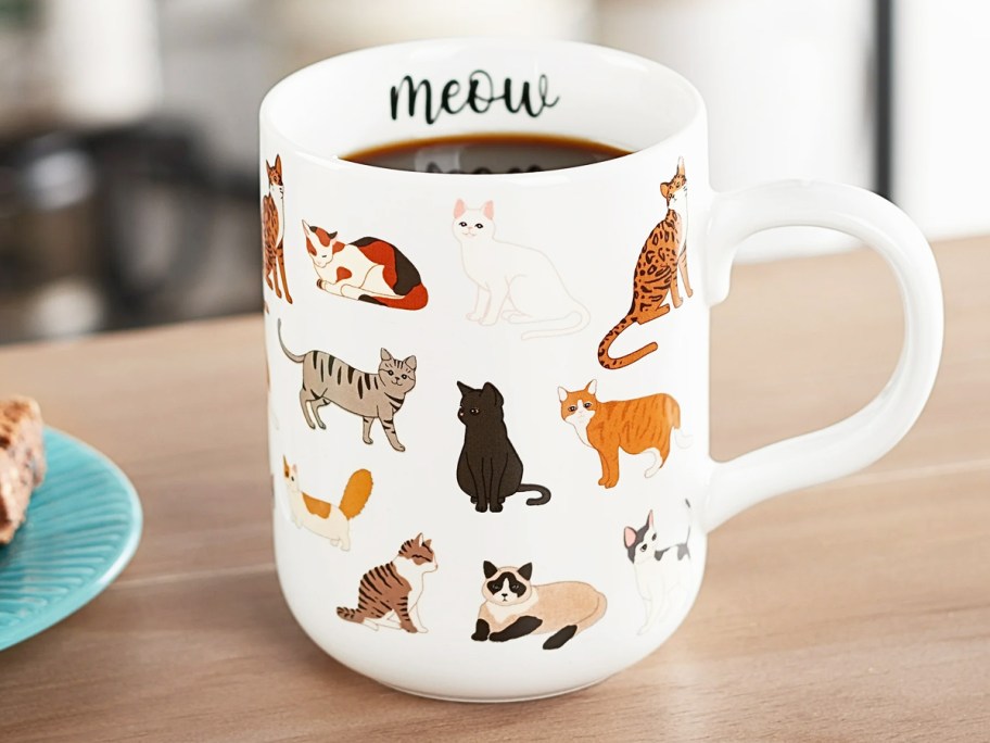 white mug covered in cats that says "meow"