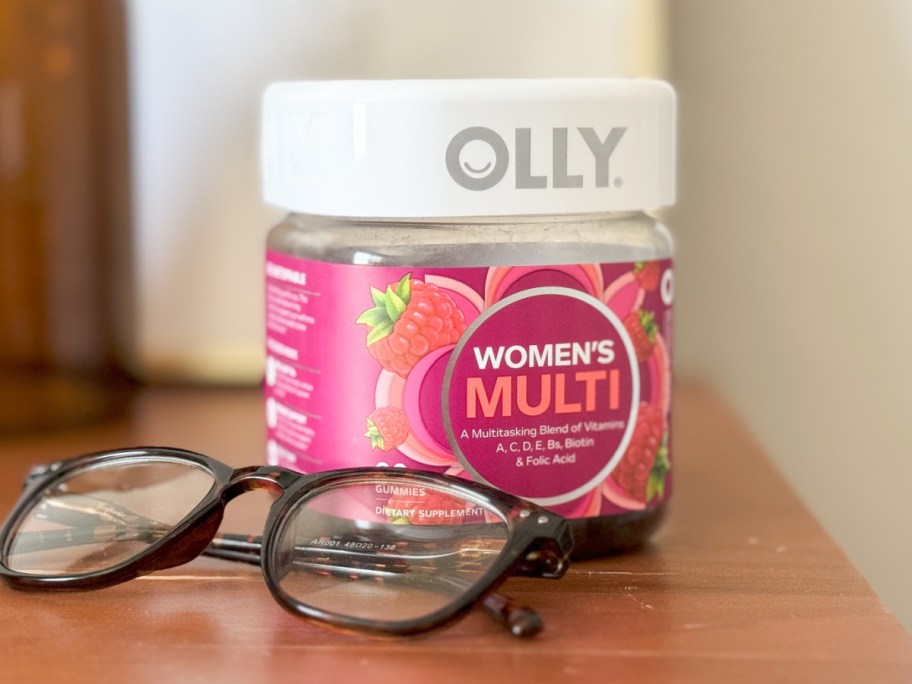 Women's gummy vitamins in plastic container on dresser near eyeglasses 