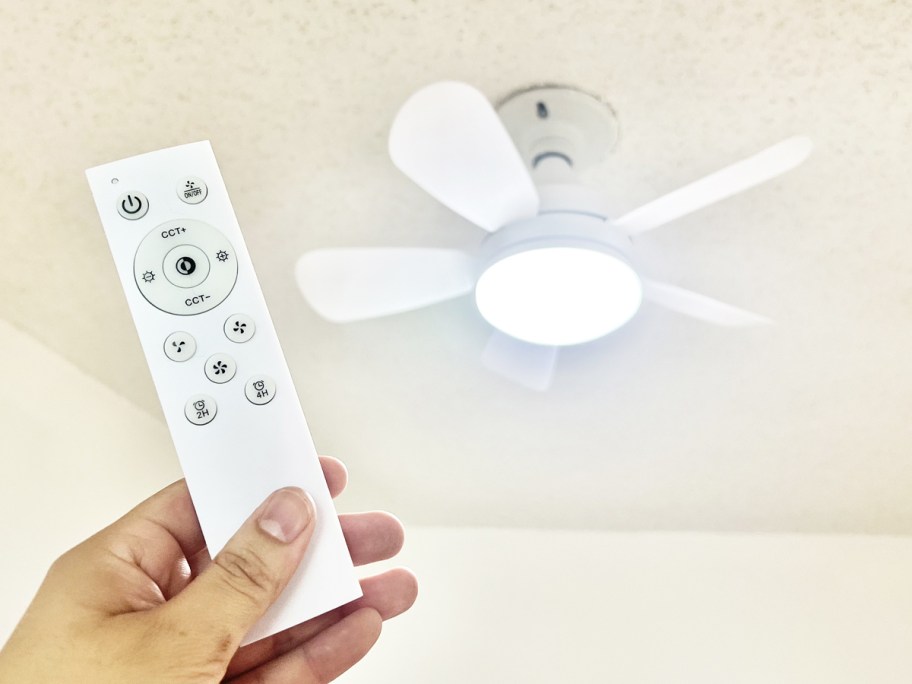 hand holding a remote in front of a white socket ceiling fan