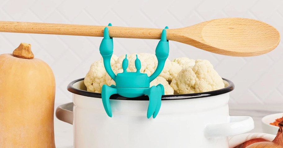 blue crab holding wooden spoon on side of pot