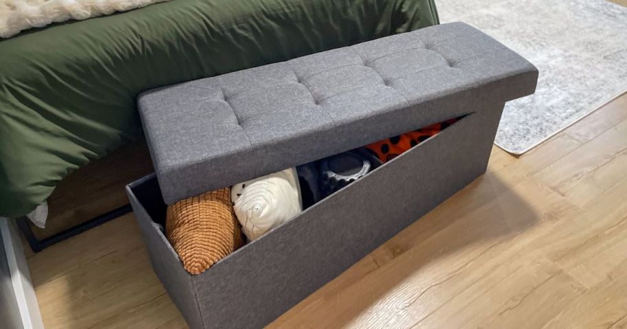 a brown fabric storage ottoman at the foot of a bed