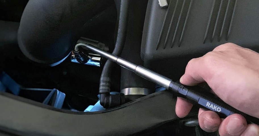 person using a magnetic pickup tool to retrieve socket from inside car