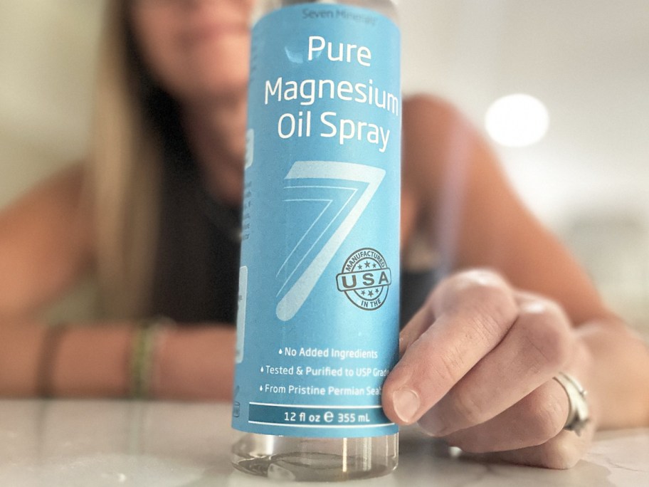 bottle of Seven Minerals Magnesium Oil Spray on counter with woman standing behind it