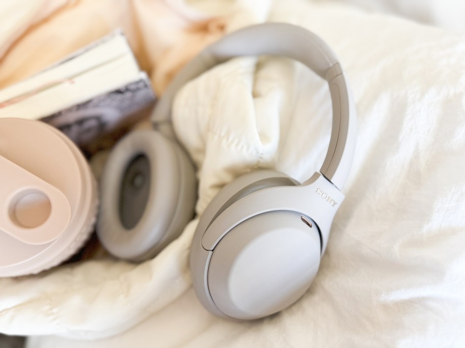 pair of silver Sony headphones on bed next to a bag with a book and water bottle in it