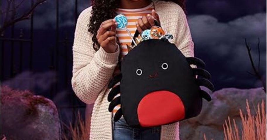 girl holding Squishmallows Original Halloween Treat Pail with candy in it