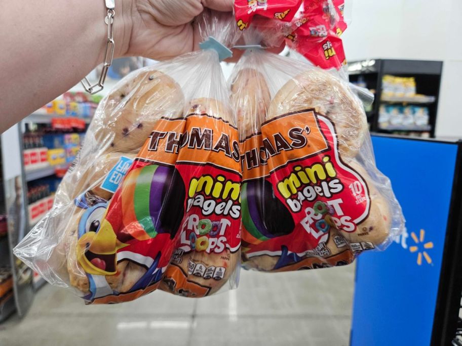 A hand holding 2 bags of Thomas Mini Bagels Froot Loops