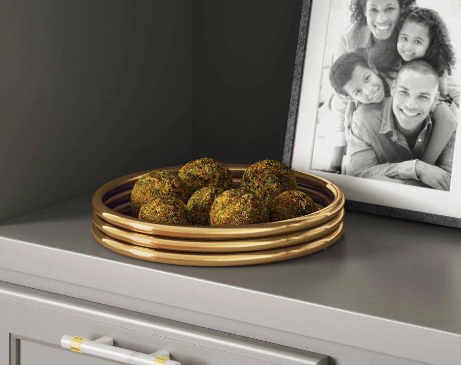 a round brass decorative tray next to a photo on a bookcase