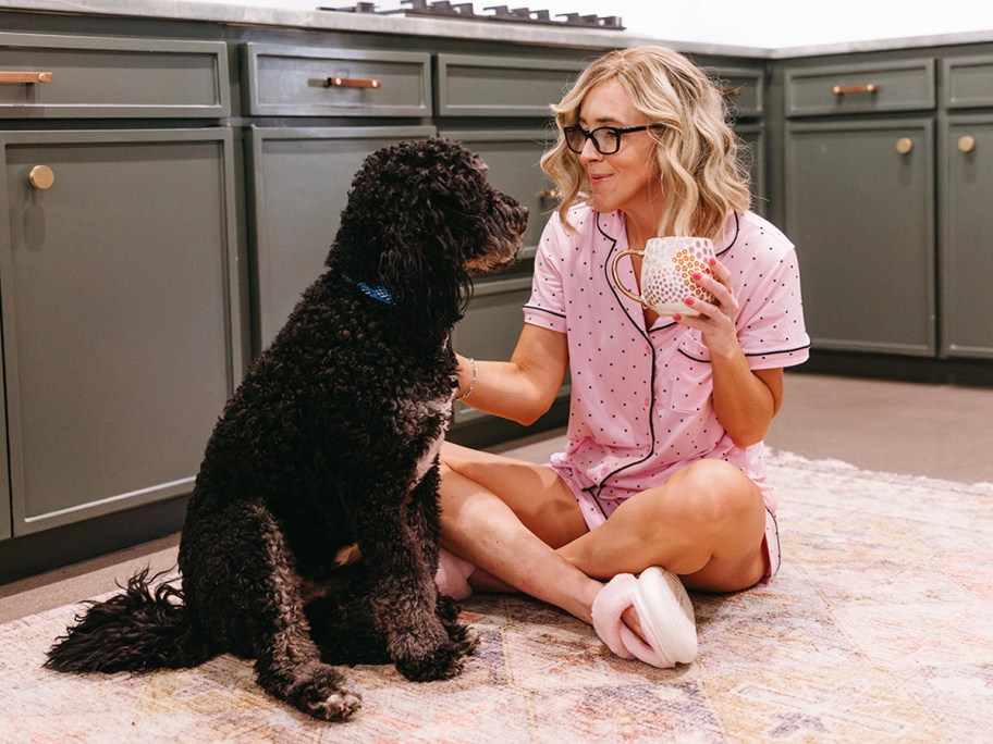 woman sitting on kitchen floor holding coffee mug and petting dog