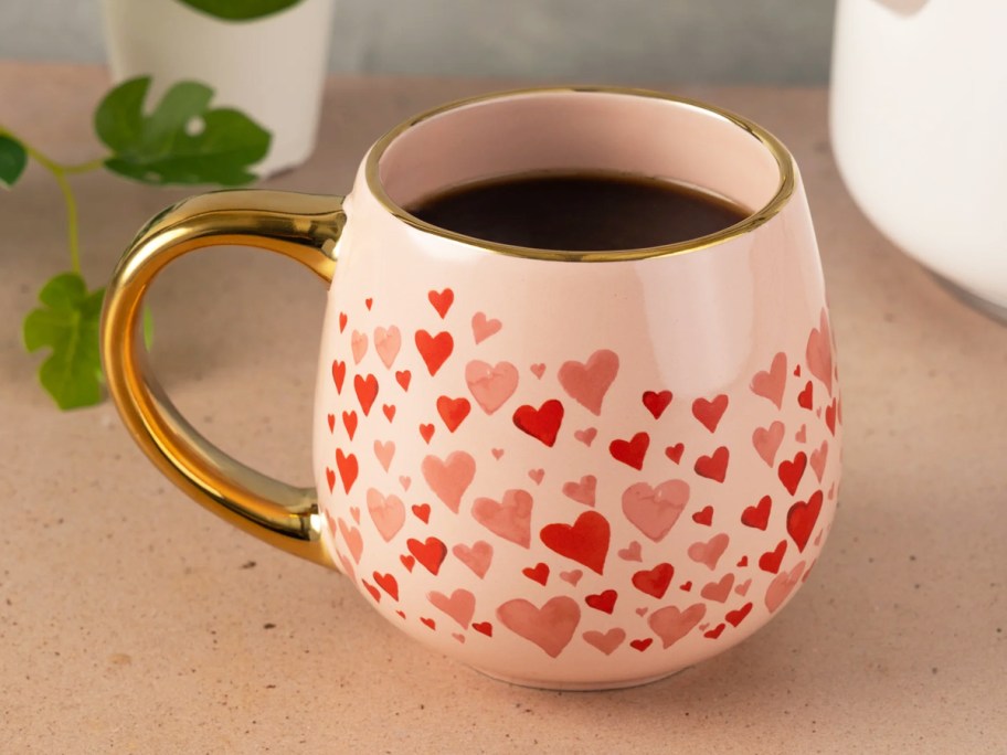 pink coffee mug with hearts print and gold handle