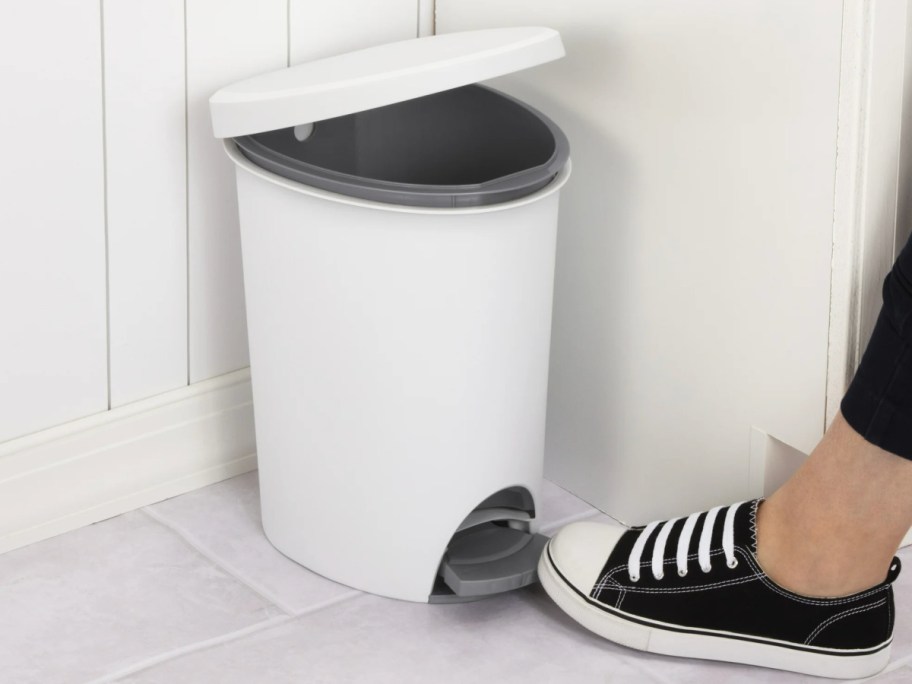 Woman stepping on bottom of white trashcan to open lid