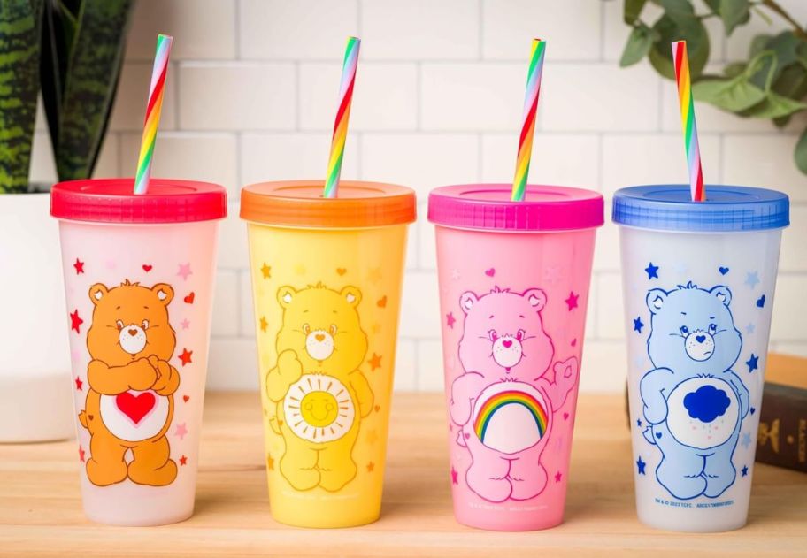 4 Care Bears tumblers with lids and straws lined up on a kitchen counter