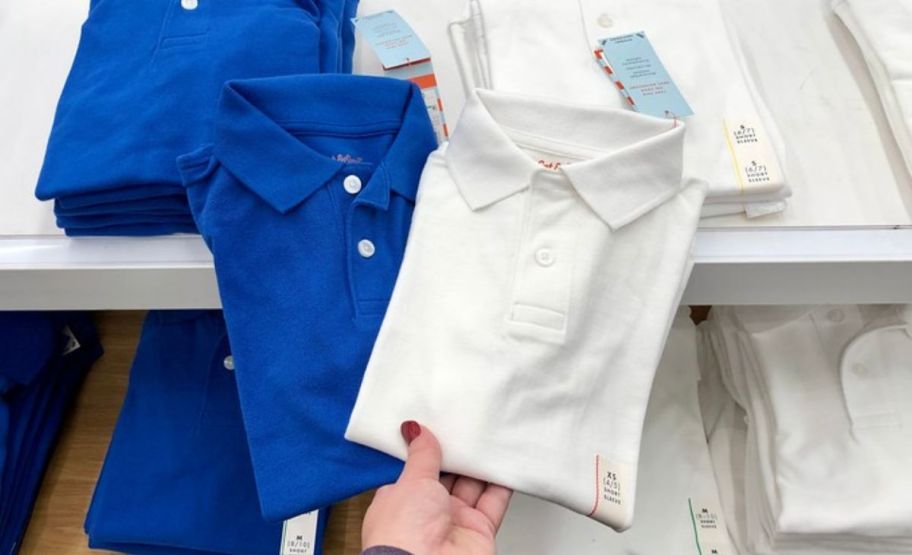 a womans hand holding 2 cat and jack school uniform polos