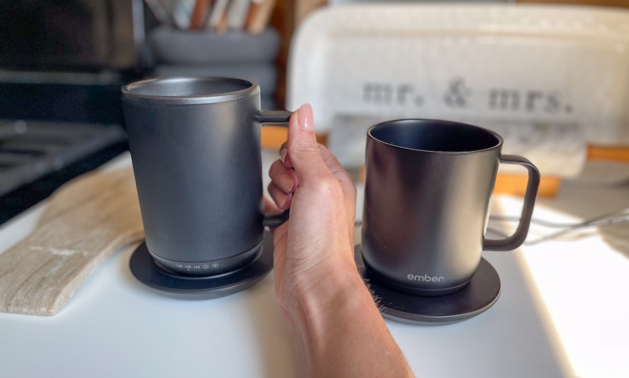 hand holding side of gray mainstays coffee mug with ember mug on counter next to it