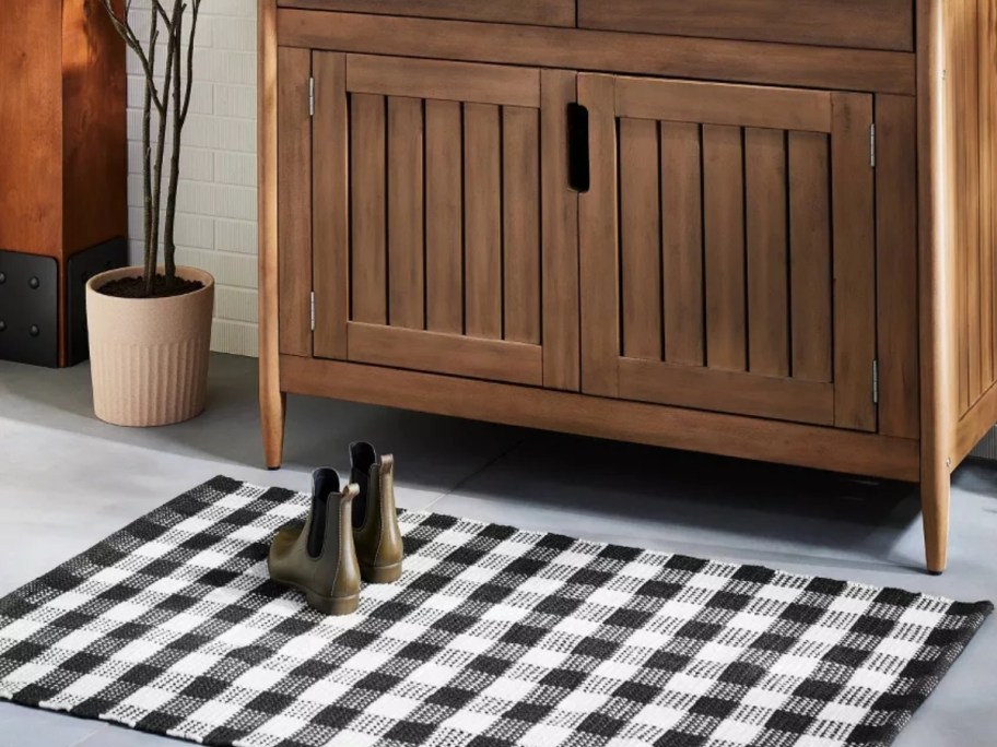 black and white gingham accent rug with boots on it in front of a buffet cabinet