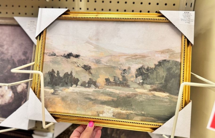 a womans hand holding a piece of framed wall decor