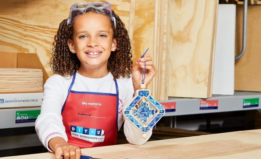 a little girl shown standing behind a table displaying a wooden spinning snowflake that she made