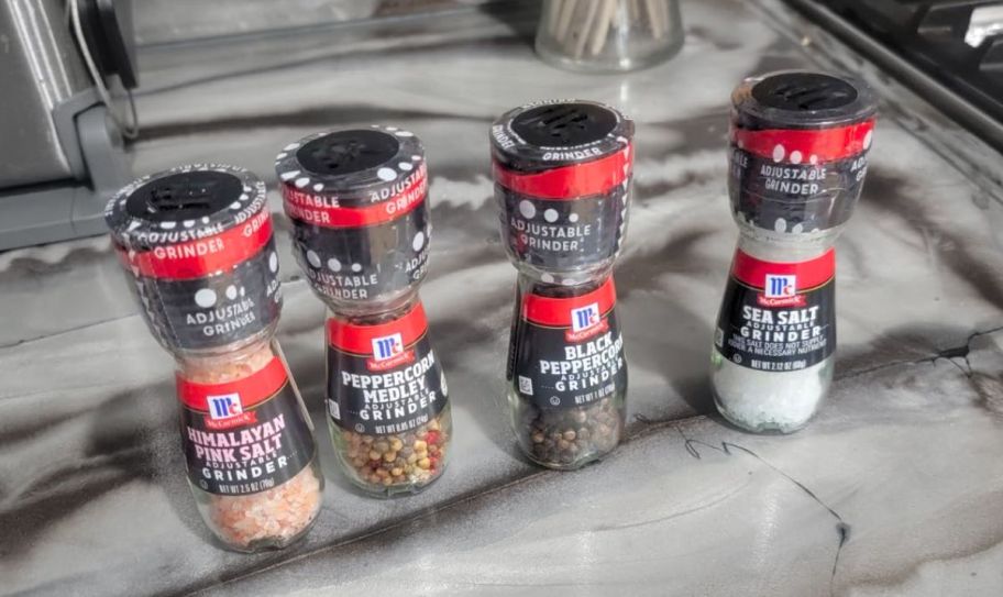 a set of 4 McCormick salt and peppercorn grinders on a marble kitchen countertop