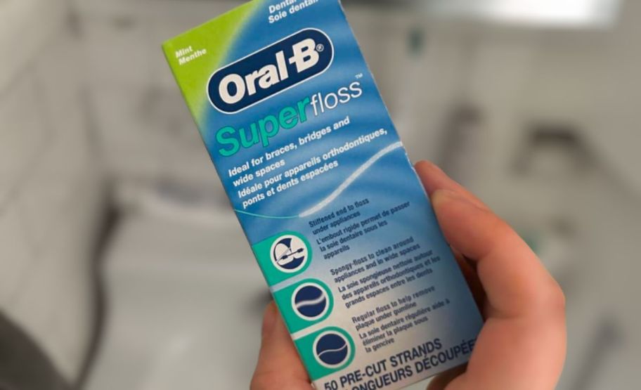 a mans hand holding a box of oral b super floss mint flavor