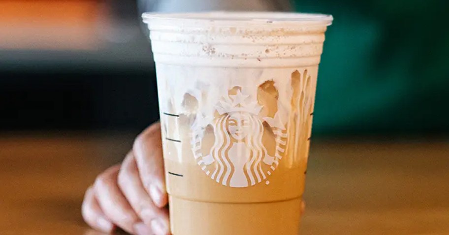 hand holding starbucks drink on table