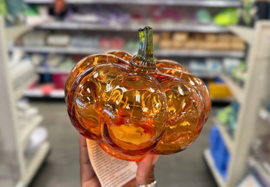 a womans hand holding an orange glass pumpkin