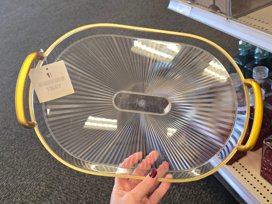 hand holding a clear and gold serving tray with handles