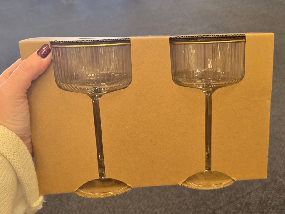 hand holding a set of 2 glass and gold Cocktail Glasses in a brown packaging