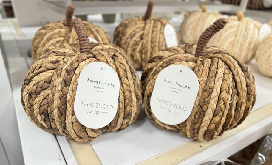 two small woven pumpkins on a store shelf with additional pumpkins in the background