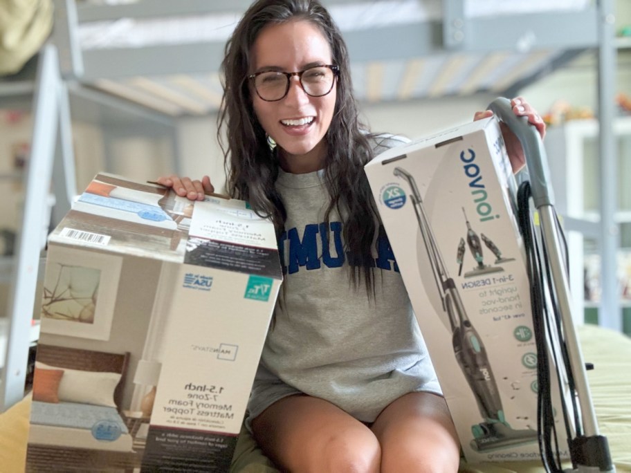 girl in sweatshirt holding vacuum and mattress topper box