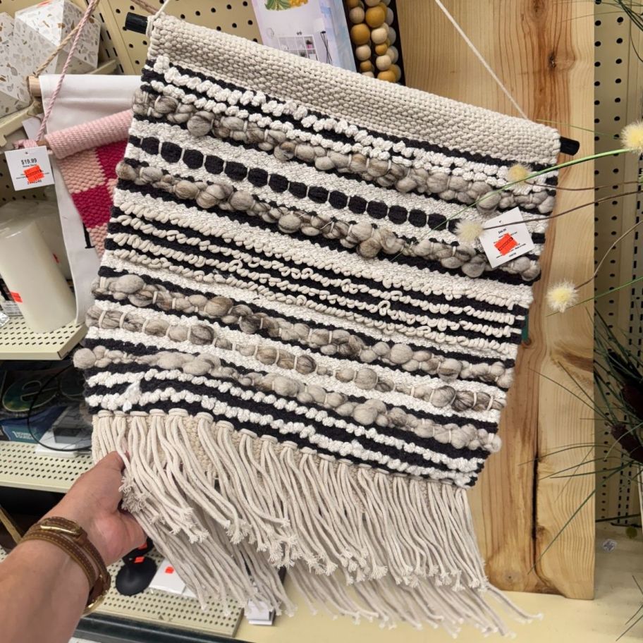 a womans hand holding a piece of woven wall decor