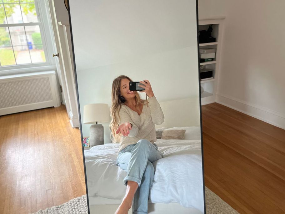 A woman sitting on a bed, looking into a BEAUTYPEAK Full Length Mirror