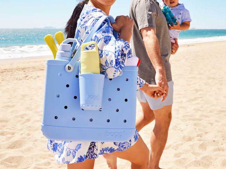 woman walking on beach holding a light blue bogg bag