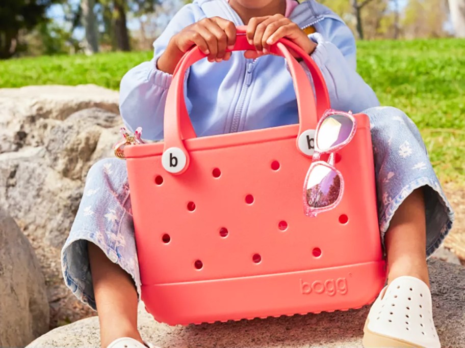 girl holding a bright pink bogg bag with sunglasses hanging on the side