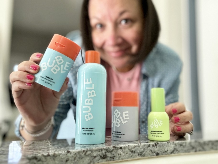 woman standing behind row of bubble skincare products on bathroom counter