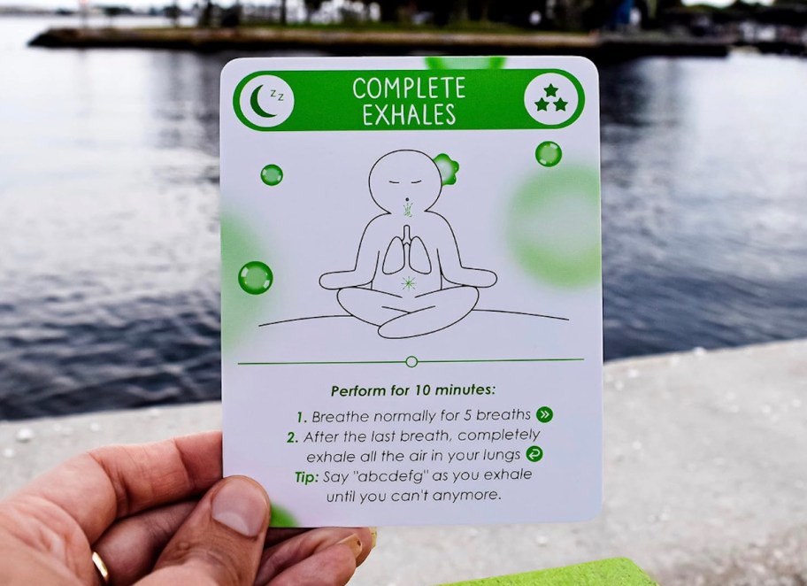 person holding Daily Meditation Card in front of lake